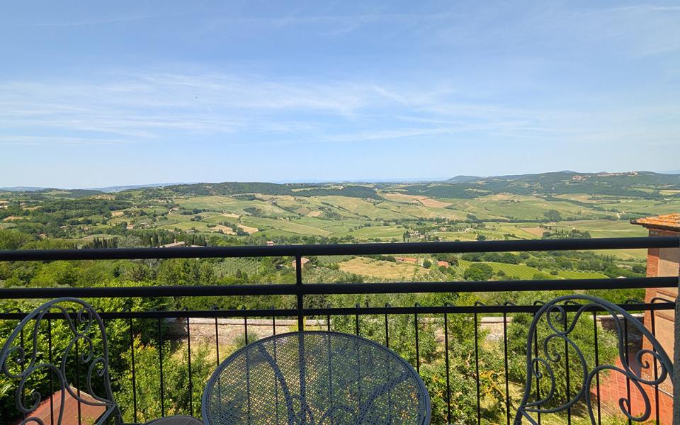 Vista panoramica su colline verdi, cielo azzurro, tavolo e sedie in ferro battuto.