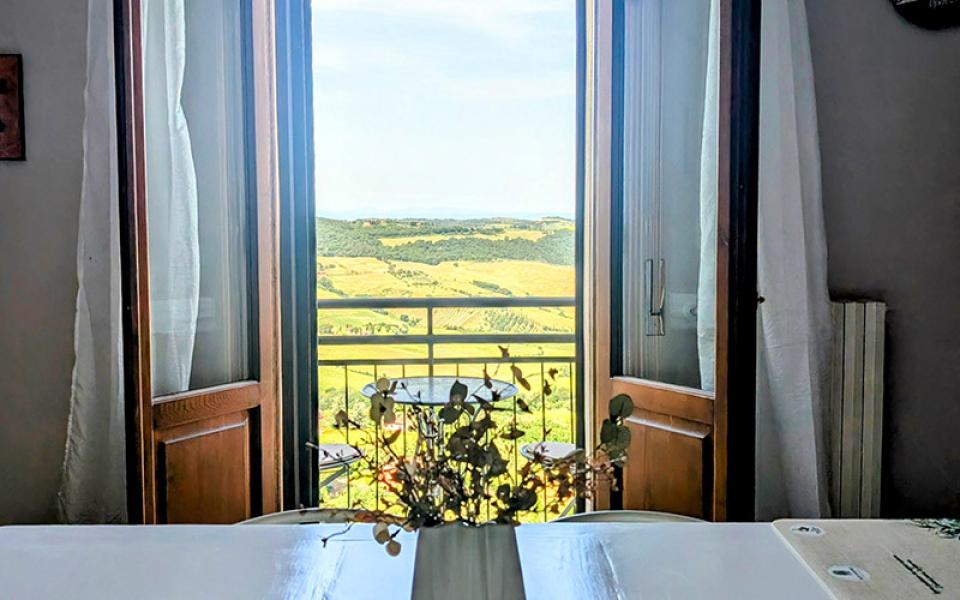 Vista mozzafiato su colline verdi da una finestra aperta, tavolo con fiori in primo piano.