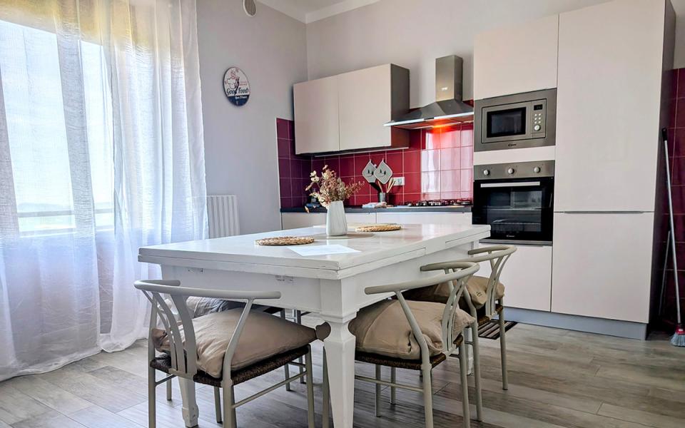 Cucina luminosa e accogliente con tavolo bianco, sedie imbottite e dettagli moderni.